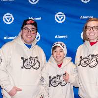 Group of three standing in front of GVSU backdrop with custom sweatshirt on